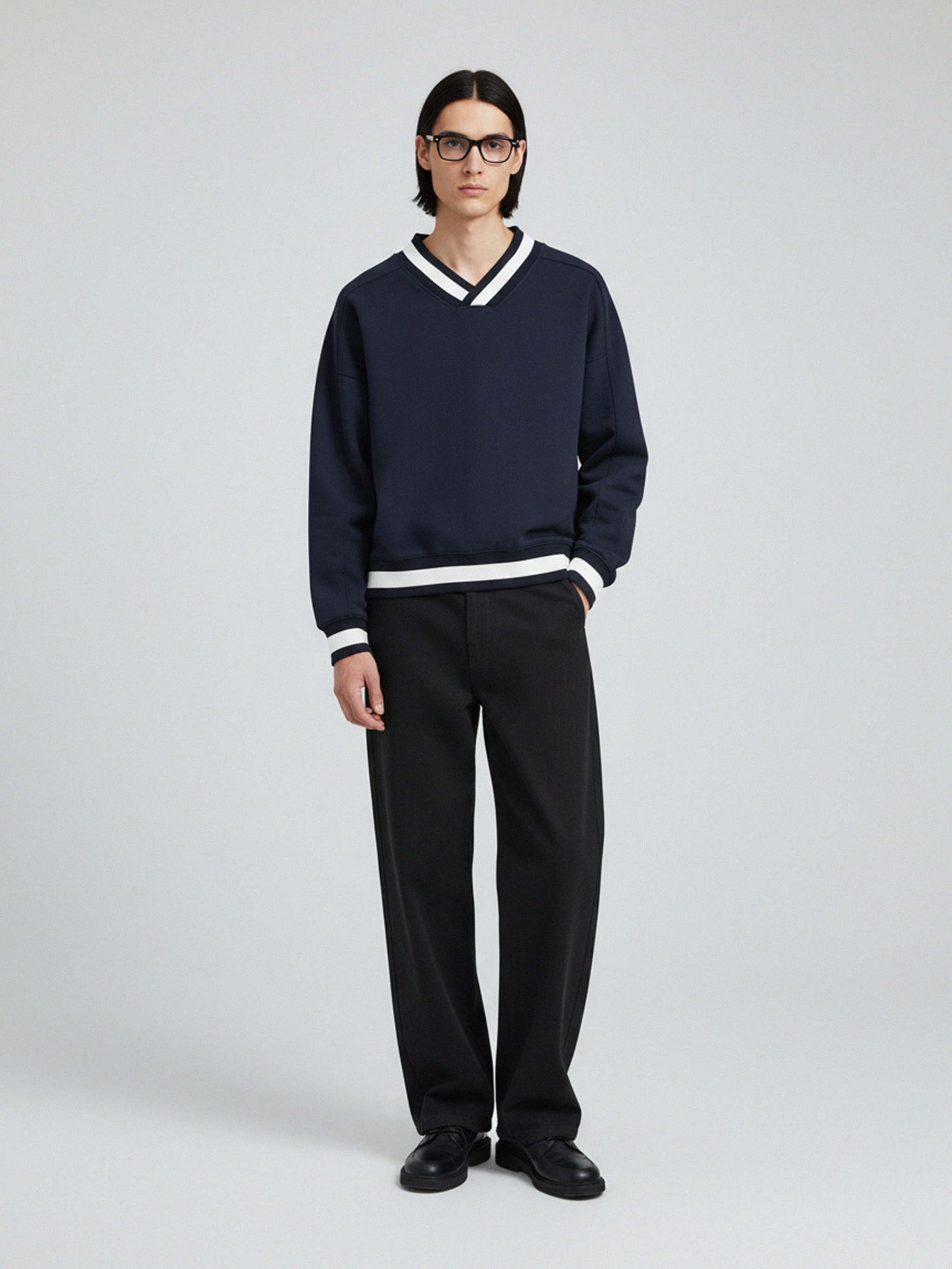 Person wearing a navy sweater with white trim and black pants on a light gray background